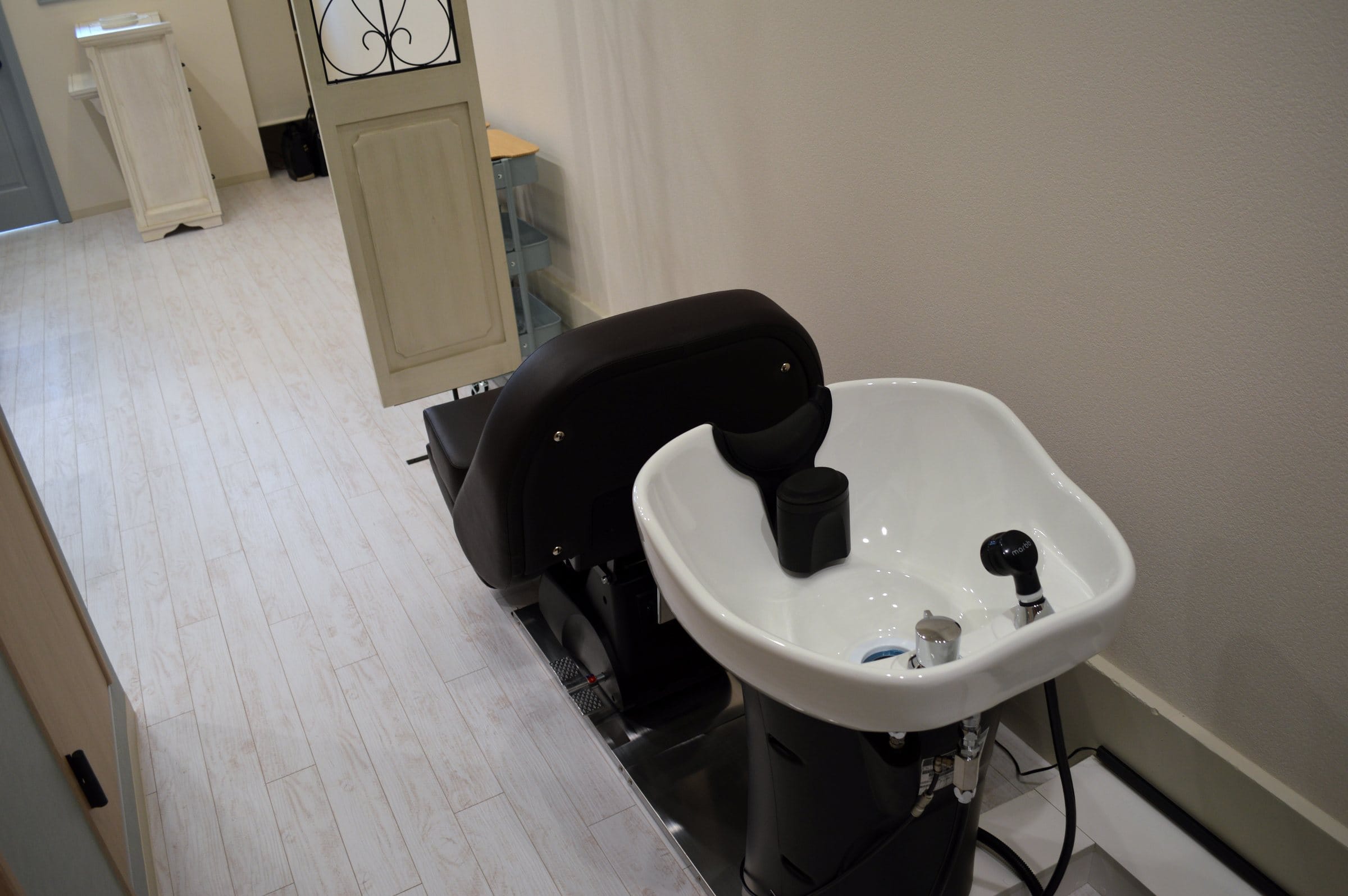 Behome のシャンプー台。黒っぽい椅子と白い洗面台